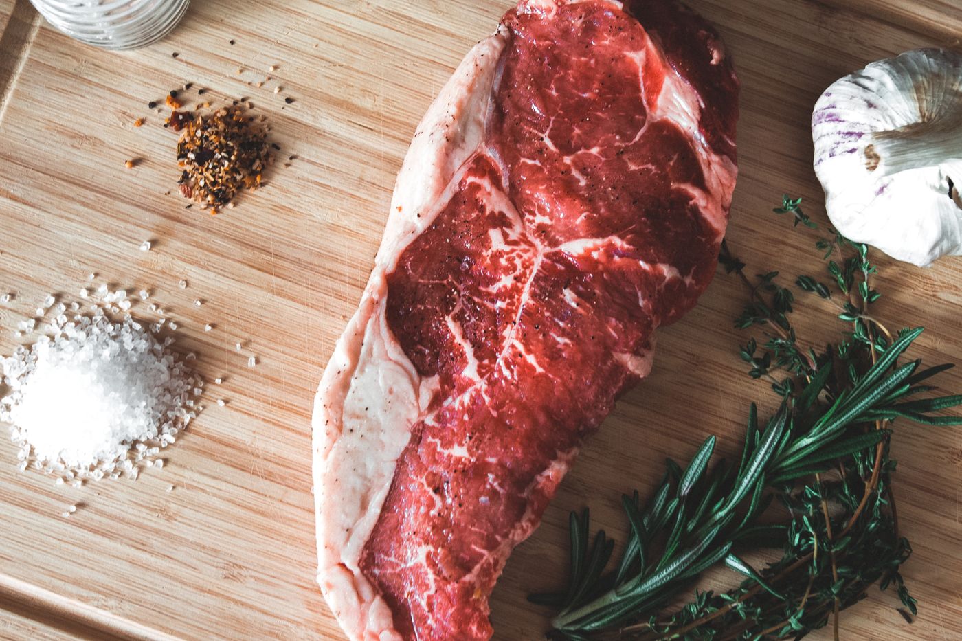 Frisches Rindersteak auf einem Holzbrett mit Rosmarin, Knoblauch und grobem Salz