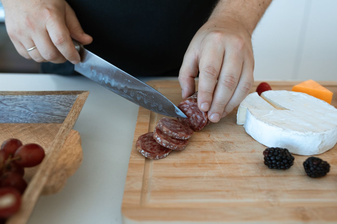 Hand schneidet Salami auf einem Holzbrett neben Käse und Beeren